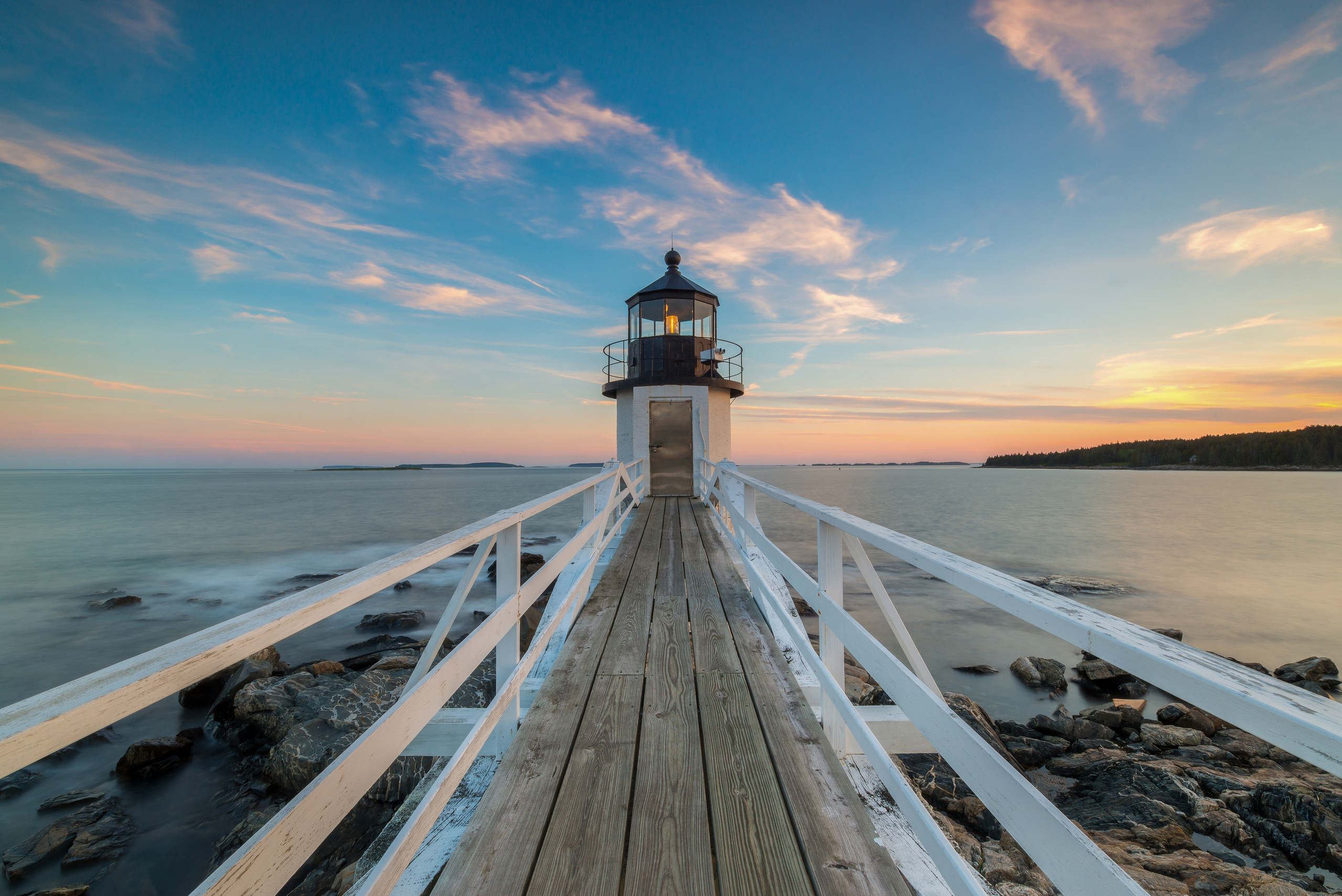 Picture of a wooden path accross boulders and the sea leading to a lighthouse